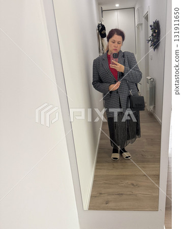 A woman posing in a hallway wearing a plaid blazer over a red sweater. Style layering, self-expression and everyday fashion reflecting individuality and urban lifestyle. A woman posing in a hallway wearing a plaid blazer over a red sweater. Style layering, self-expression and everyday fashion reflecting individuality and urban lifestyle. 131911650