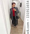 A woman posing in a hallway wearing a plaid blazer over a red sweater. Style layering, self-expression and everyday fashion reflecting individuality and urban lifestyle. 131911654
