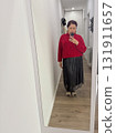 A woman standing in a hallway wearing a red sweater and metallic skirt. Everyday mood, quiet confidence and casual indoor atmosphere in modern home interior. 131911657