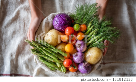 Fresh produce including potatoes, tomatoes, and asparagus arranged in a reusable basket on a table 131912133