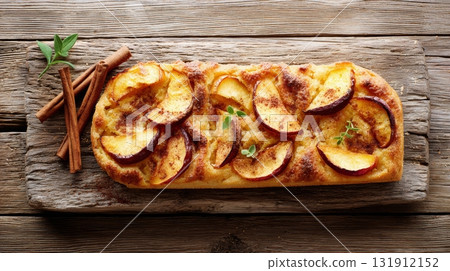 Delicious focaccia bread topped with caramelized apple slices rests on a rustic wooden surface, perfect for autumn celebrations 131912152