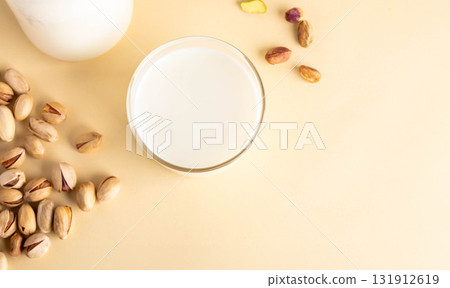 Pistachios and glass of milk on soft beige background with scattered nuts Top view Copy space Pistachios and glass of milk on soft beige background with scattered nuts Top view Copy space 131912619