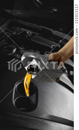Technician hand pouring golden engine oil from plastic container into car motor Technician hand pouring golden engine oil from plastic container into car motor 131913117