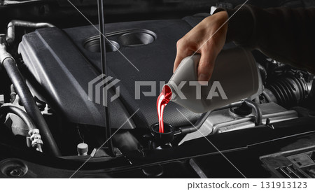 Mechanic hand pouring red transmission fluid into car engine under hood close up Mechanic hand pouring red transmission fluid into car engine under hood close up 131913123