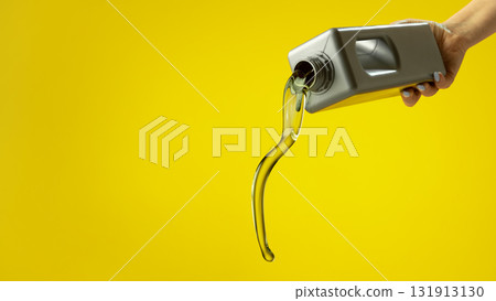 Stream of golden motor oil pouring from plastic container on yellow background 131913130