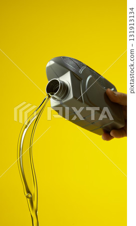 Silver bottle with dynamic stream of motor oil isolated on yellow studio background Silver bottle with dynamic stream of motor oil isolated on yellow studio background 131913134