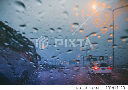 Driving on a rain-slicked highway at twilight, viewed through a wet car windshield with blurred traffic and orange streetlights 131913423