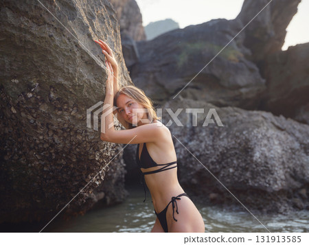 Young woman enjoying serene evening at sea in Krabi, Thailand during sunset. Calm waves, golden light, and peaceful atmosphere highlight tropical beauty and connection with nature. 131913585