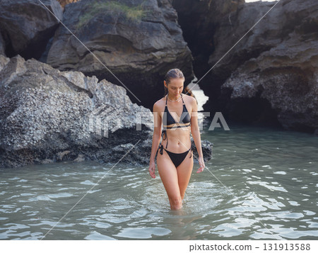 Young woman enjoying serene evening at sea in Krabi, Thailand during sunset. Calm waves, golden light, and peaceful atmosphere highlight tropical beauty and connection with nature. 131913588