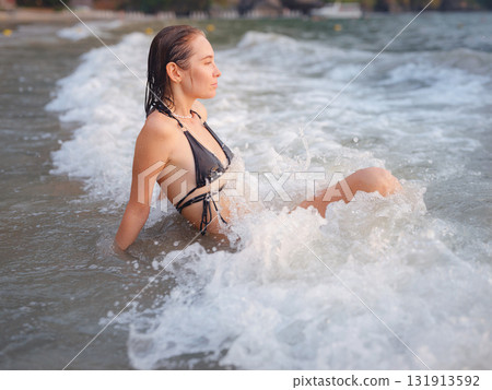 Young woman enjoying serene evening at sea in Krabi, Thailand during sunset. Calm waves, golden light, and peaceful atmosphere highlight tropical beauty and connection with nature. 131913592
