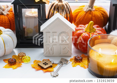 Cozy layout on a wooden background of slats with pumpkins, autumn leaves, a tiny house and keys - autumn mood, Halloween, housing, relocation, mortgage, insurance. 131913659
