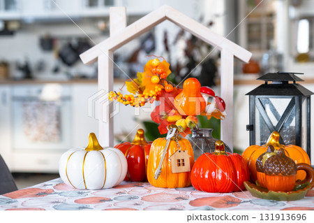 Cozy autumn decor on white kitchen with tiny house and keys, pumpkins, autumn leaves, autumn mood, Halloween, Harvest Festival, housing, relocation, mortgage, insurance. 131913696