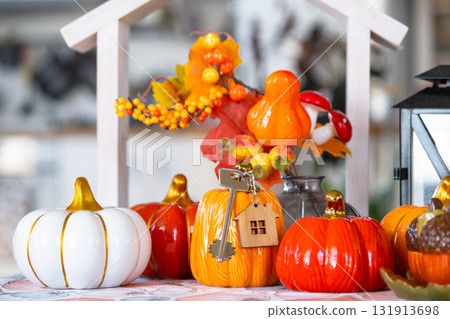 Cozy autumn decor on white kitchen with tiny house and keys, pumpkins, autumn leaves, autumn mood, Halloween, Harvest Festival, housing, relocation, mortgage, insurance. 131913698