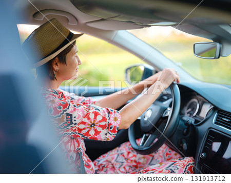 Young woman drives through scenic countryside, hands on wheel, focused on road ahead. Peaceful summer journey through rural landscapes captures freedom and adventure. Croatia, Europe 131913712