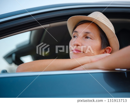 Traveler woman in red ethnic dress and hat drives car through scenic countryside of Croatia in summer. Surrounded by lush fields and forests, she enjoys peaceful and adventurous road trip 131913713