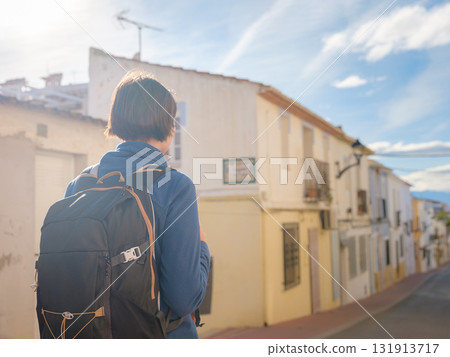 Young woman strolling through charming narrow streets of Denia, Alicante province, Spain, surrounded by historic Mediterranean architecture , enjoying peaceful atmosphere and cultural ambiance. 131913717