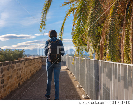 Young woman exploring historic castle in Denia, Alicante province, Spain, scenic views of town below, set against cooler season backdrop. blend of history and tranquility in timeless setting. Young woman exploring historic castle in Denia, Alicante province, Spain, scenic views of town below, set against cooler season backdrop. blend of history and tranquility in timeless setting. 131913718