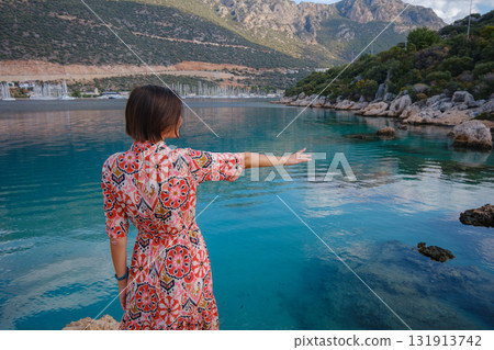 Woman stands on Mediterranean Sea coast, embracing cool, off-season atmosphere with waves crashing on shore and overcast sky above. serene, peaceful moment on quiet beach. Woman stands on Mediterranean Sea coast, embracing cool, off-season atmosphere with waves crashing on shore and overcast sky above. serene, peaceful moment on quiet beach. 131913742