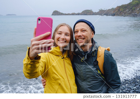 Couple enjoys Turkish coastline and taking selfie on beach in Winter. walking on stones, watching sea waves, relaxing together, slow romantic moment near calm blue water under soft winter light. Couple enjoys Turkish coastline and taking selfie on beach in Winter. walking on stones, watching sea waves, relaxing together, slow romantic moment near calm blue water under soft winter light. 131913777