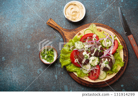 Preparing and cooking falafel wrap on pita on wooden cutting board with hummus top view, space for text 131914299