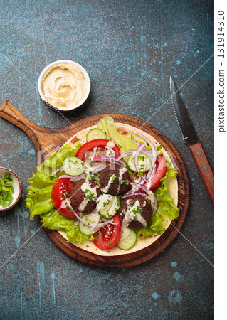 Preparing and cooking falafel wrap on pita on wooden cutting board with hummus top view Preparing and cooking falafel wrap on pita on wooden cutting board with hummus top view 131914310