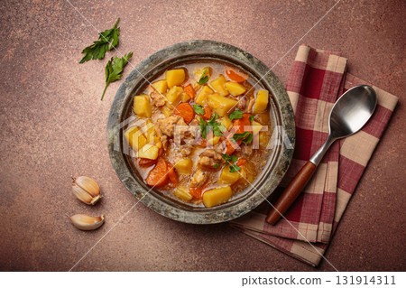 Chicken stew or soup with potatoes and carrots served in rustic bowl with spoon top view on dark brown concrete background Chicken stew or soup with potatoes and carrots served in rustic bowl with spoon top view on dark brown concrete background 131914311