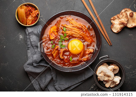 Traditional Korean kimchi jjigae hot soup or stew with egg yolk in black rustic bowl on dark background top view 131914315