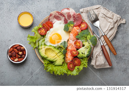 Balanced ketogenic diet meal with salmon, avocado, egg, bacon and vegetables on plate with cutlery top view on grey background Balanced ketogenic diet meal with salmon, avocado, egg, bacon and vegetables on plate with cutlery top view on grey background 131914317