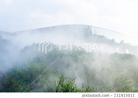 Artificial fog in a modern park with a mirrored wall of a futuristic building in the background Artificial fog in a modern park with a mirrored wall of a futuristic building in the background 131915011