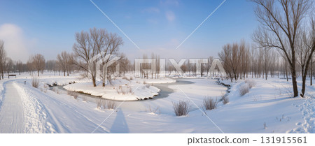 Winter landscape with a frozen river winding through a snow-covered park with bare trees and clear blue sky. Peaceful seasonal outdoor scenery. 131915561