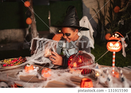 Young girl wearing witch costume looking at Halloween decorations at night 131915590