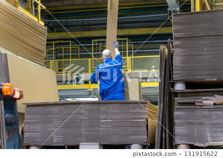 a worker handles a large sheet of corrugated cardboard a worker handles a large sheet of corrugated cardboard 131915622