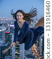 Woman in a blue dress is flying on a broomstick in a city at night 131916460
