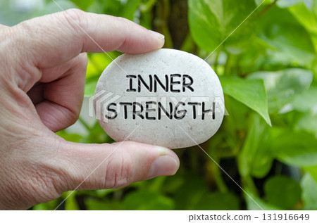 Hand holding a white stone with INNER STRENGTH text engraved on it, representing life purpose of resilience and personal power 131916649