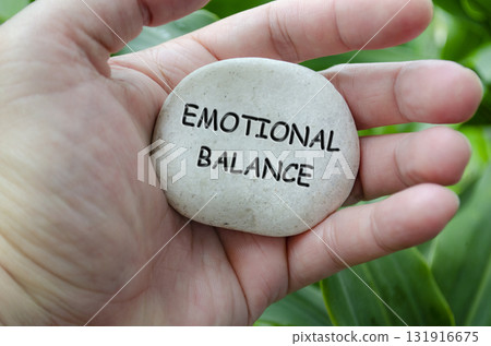 Hand holding a white stone with EMOTIONAL BALANCE text engraved on it, reflecting life purpose of mental harmony and control Hand holding a white stone with EMOTIONAL BALANCE text engraved on it, reflecting life purpose of mental harmony and control 131916675