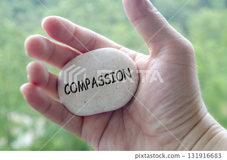 Hand holding a white stone with COMPASSION text engraved on it, representing life purpose of empathy and love for others 131916683
