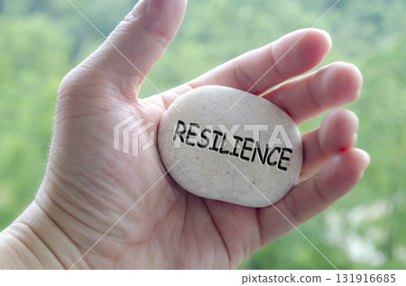 Hand holding a white stone with RESILIENCE text engraved on it, reflecting life purpose of endurance and emotional strength Hand holding a white stone with RESILIENCE text engraved on it, reflecting life purpose of endurance and emotional strength 131916685