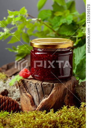 A jar of raspberry jam with fresh berries on an old tree trunk in the forest. 131916878