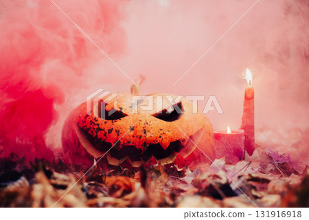 Halloween pumpkin head and glowing candles on autumn foliage. Creepy and scary atmosphere, red smoke on the background Halloween pumpkin head and glowing candles on autumn foliage. Creepy and scary atmosphere, red smoke on the background 131916918