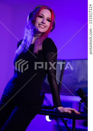 Young woman gaming in vibrant-lit setup with headset and smile 131917124