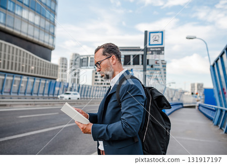 Mature man reading while waiting for bus. Mature man reading while waiting for bus. 131917197