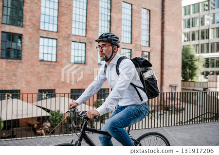 Man riding bike to work in city with helmet and backpack 131917206