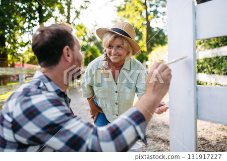 Mature son helping senior mother on farm, painting fence. Mature son helping senior mother on farm, painting fence. 131917227