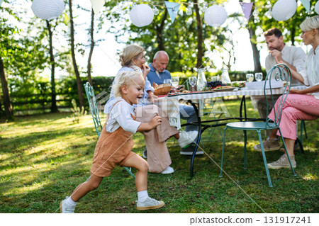 Toddler boy running around table at family garden party. Toddler boy running around table at family garden party. 131917241