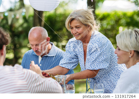 Senior woman serving grilled food during family grill party. 131917264