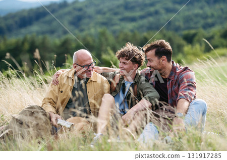 Grandfather, father and teen boy hiking togeter in nature, resting on meadow. Grandfather, father and teen boy hiking togeter in nature, resting on meadow. 131917285