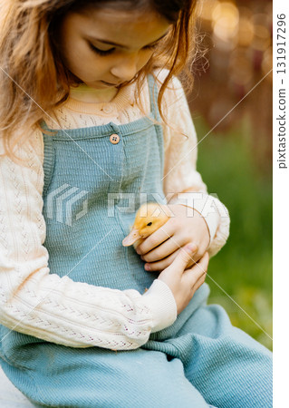 Young girl in garden playing with baby duckling. 131917296
