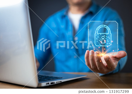 A man in a blue shirt holds a glowing digital lock hologram in front of a laptop, symbolizing secure cyber data protection.Lock icon and network nodes represent advanced security technology. A man in a blue shirt holds a glowing digital lock hologram in front of a laptop, symbolizing secure cyber data protection.Lock icon and network nodes represent advanced security technology. 131917299