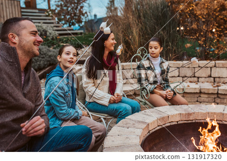 Family roasting marshmallows over open flame, campfire on backyard. 131917320