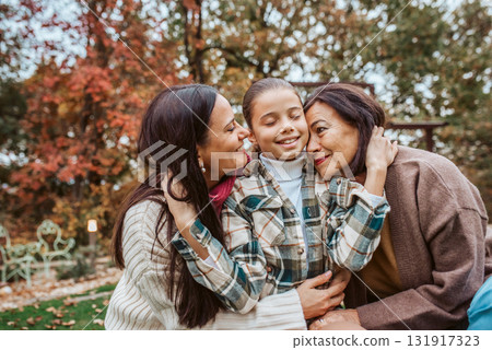 Mother, grandmother and granddaugter standing in autumn garden. 131917323